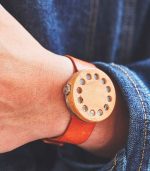 A person wearing an orange leather bracelet with holes.